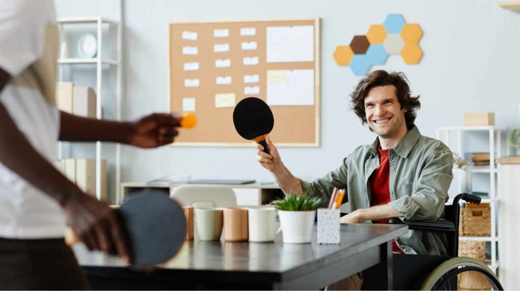 Smiling man in a wheelchair playing table tennis in an office setting