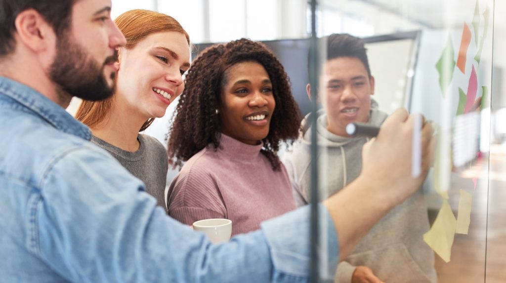 Smiling coworkers together at a glass whiteboard
