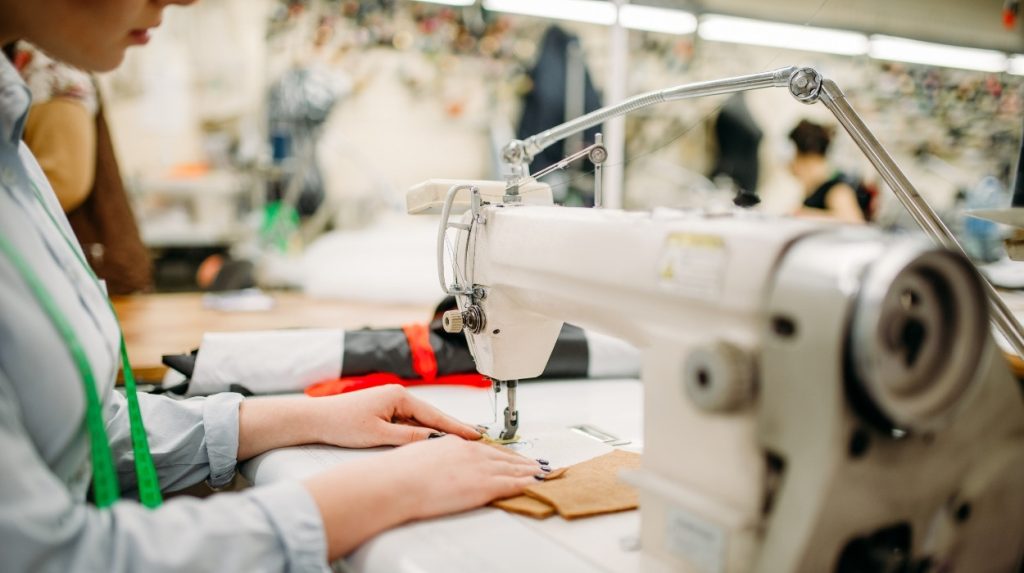 Woman at a sewing machine in a busy-looking workroom