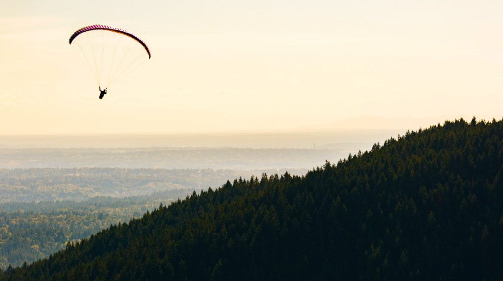 Paraglider soaring over a forested hillside with a misty landscape in the background